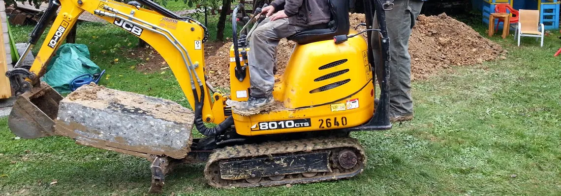 Bagger transportiert Bruchstück der Betonwand beim Praxisneubau 